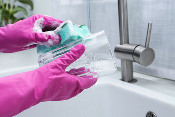 Woman washing glass with sponge above sink in kitchen, closeup