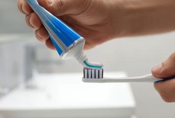 Man applying toothpaste on brush in bathroom, closeup