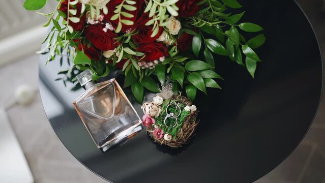 On the table is a composition of perfumes, flowers and gold rings. View of objects from above