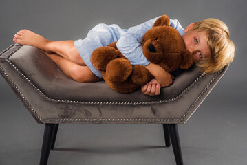 Sleepy little boy lying down on a chair while cuddling with his stuffed bear 