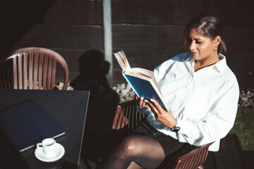 A portrait of a pensive mature plus-size Hispanic woman reading a book while sitting in an outdoor...