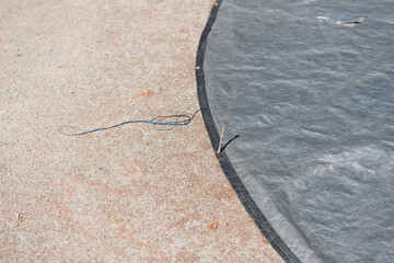 detail of a gray tarpaulin held in place by spikes (over the pitcher's mound at the community...