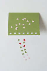 small pink, green, and red hearts and card on blank paper