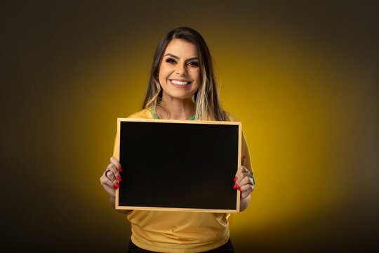 Brazilian fan holding a blackboard. Woman fan celebrating in soccer or soccer match on yellow background. Brazil colors.