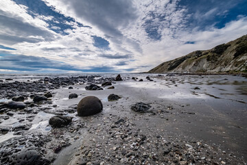 Obraz premium Rocks and pebbles on an ocean beach at low tide under a cloudy sky