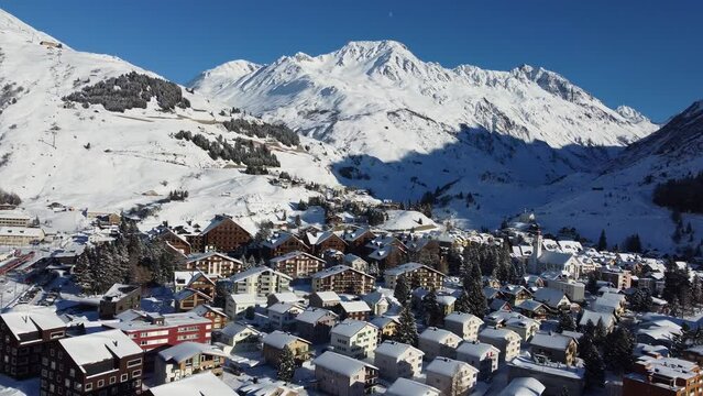 Andermatt, Switzerland: Aerial drone footage of the idyllic mountain village of Andermatt in the Swiss alps in winter in Canton Uri on a sunny day after a snow fall. 