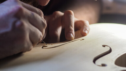 luthier violin maker working on the f holes on a raw new violin