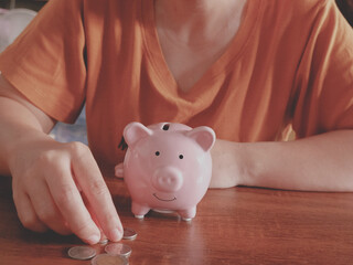 woman hand putting money coin into piggy for saving money wealth and financial concept on wood table