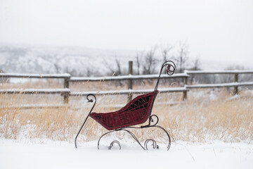 Antique baby sled pram in snowy Winter field as it is snowing with an old primitive wooden fence...