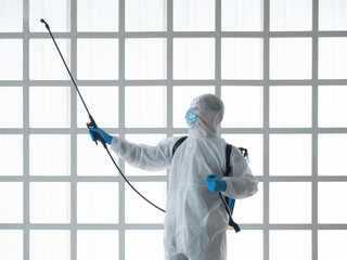 Asian cleaner man in white uniform, hygiene mask and gloves use gun spray sanitizer for anti bacteria at warehouse company
