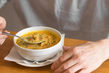 Man eating Thai curry soup with chicken in cafe. Man's hand holds a full spoon over a bowl of soup on a wooden table.