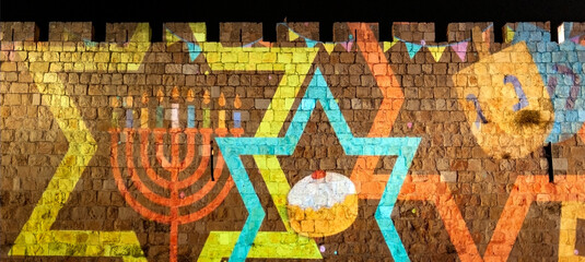 Colorful symbols of the Jewish holiday of Hanukkah are projected on the ancient stone walls of the Old City of Jerusalem, Israel. © Yehoshua Halevi