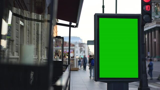 4k People walk and green mockup poster stands on city street spbd. Empty advertising billboard standing by old building, pedestrians walking casually in open air on summer day. Large light box display