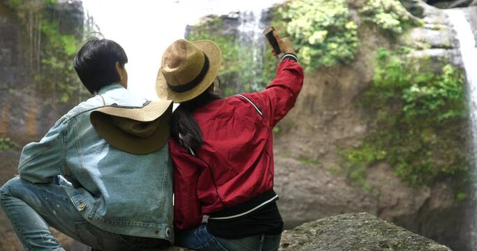 Tourist couple taking a selfie against beautiful waterfall background, Hikers with waterfall