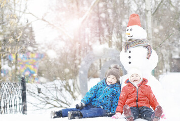 Children in the park in winter. Kids play with snow on the playground. They sculpt snowmen and slide down the hills.