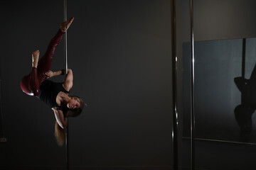 The dancer on the pylon in the studio. Girl doing exercises on a sports equipment.