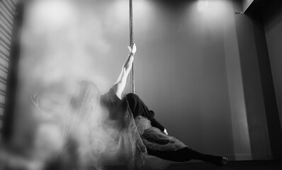 The dancer on the pylon in the studio. Girl doing exercises on a sports equipment.