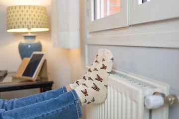 Woman with her feet resting on a radiator to warm them up by the cold of winter and energy saving.