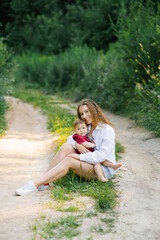 Naklejka premium Smiling mom holds her little son in her arms, sitting in the park on the path