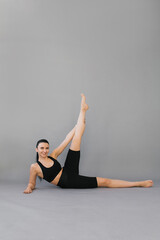Woman does sports. A brunette in black sportswear is doing an exercise from yoga or fitness, she is lying on her side with her leg raised, isolated gray background