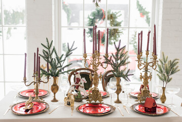 Christmas serving of a festive New Year's dinner. Candles in candlesticks, spruce branches, red and gold plates