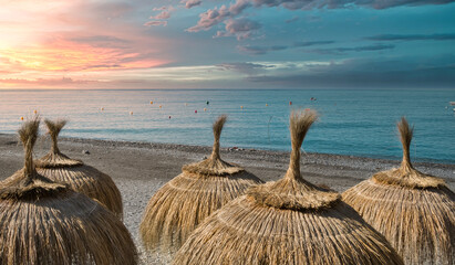 Sombrillas hechas con hojas secas de palmera en la playa de Almuñecar con el mar Mediterráneo de...