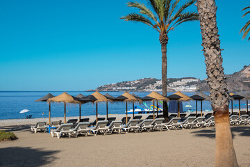Sombrillas y tumbonas en la playa de Almuñecar bañada por el agua del mar Mediterráneo, España