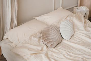 Fototapeta na wymiar Pillows in the form of seashells lie on a light bed in the bedroom