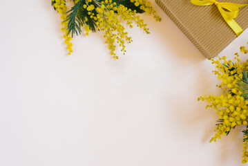 Gift with yellow mimosa flowers on a light background. Top view, flat lady, copy space
