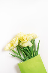 Green paper bag with spring flowers of yellow tulips on a white background. Flat lay, top view, copy space