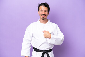 Young caucasian man doing karate isolated on purple background with surprise facial expression