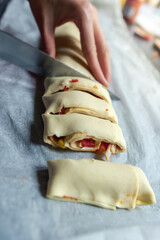 Female hands cut the rolled puff pastry into equal pieces. In the middle, there is a pepper, ham, garlic sauce, and corn. Preparing snacks for a party