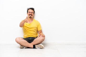 Fototapeta premium Young caucasian man sitting on the floor isolated on white background shaking hands for closing a good deal