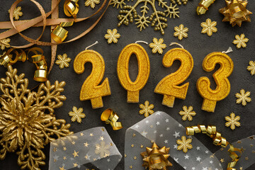 Merry Christmas and Happy New Year 2023, 2023 cake candles and various holiday decorations and ribbons in gold color on black background