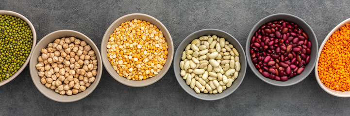 Banner of different types of legumes in bowls, yellow peas and chickpeas , colored beans and maash and lentils, top view, copy space