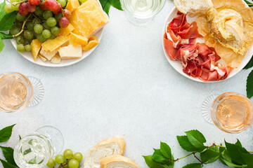 Top view of table with rose and white wine in glasses, plates with grapes, cheese and jamon, baked camembert cheese and baguette, tasting party or cozy dinner with wine