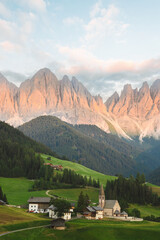 Stunning view of the Funes Valley (Val di Funes) with the Santa Maddalena Church and the mountain range of the Puez Odle Nature Park in the distance during a beautiful sunset.