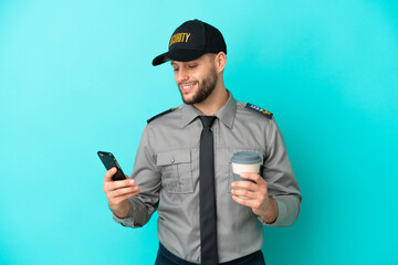 Young security man isolated on blue background holding coffee to take away and a mobile