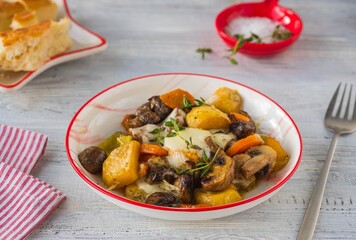 Baked vegetable mix of carrots, turnips and onions with mushrooms and cheese in a white plate on a light wooden background. Vegetable recipes.