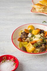 Baked vegetable mix of carrots, turnips and onions with mushrooms and cheese in a white plate on a light wooden background. Vegetable recipes.
