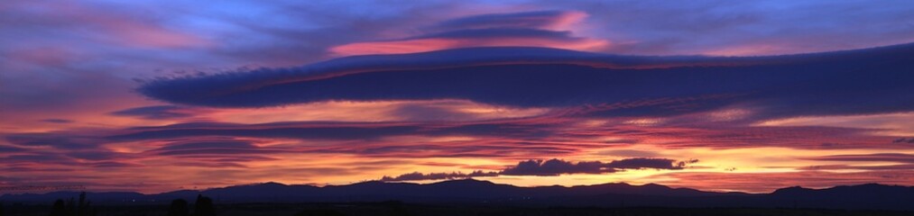 Obraz premium Atardecer en la Sierra de Guadarrama en Madrid, España. Cielo anaranjado y azul con una nube lenticular sobre la silueta de las montañas situadas al norte de Madrid.