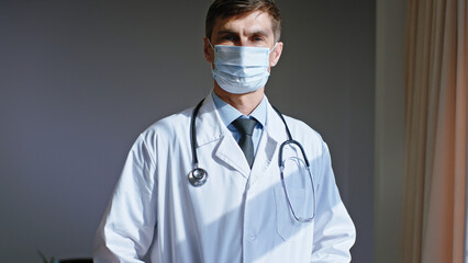 Concentrated portrait of a man doctor looking straight to the camera then looking to the window he wearing a protective mask