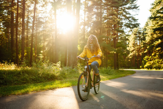 Beautiful Happy Woman In Yellow Coat Riding Bicycle In Autumn Park. Autumn Fashion. Lifestyle. Relax, Nature Concept.