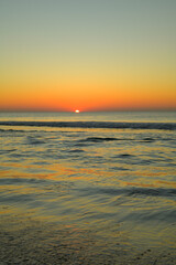 Die Sonne ist fast am Meereshorizont unter gegangen, während die seichten Wellen an den Strand...
