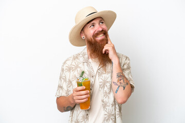 Redhead man with long beard drinking a cocktail on a beach isolated on white background thinking an idea while looking up