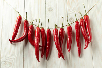 Red hot chili peppers are dried on a thread. On a white wooden background.