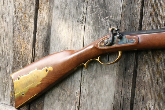 A close-up of the percussion lock and the stock of a Kentucky rifle on an old plank background