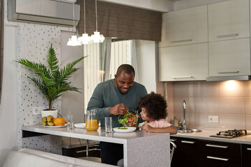 Man put salad in plate of son during have lunch