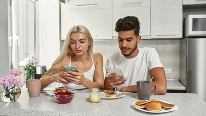 Obraz na płótnie Canvas Couple using smartphones during breakfast at table