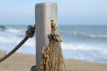 Wooden platform on the seashore. Fence made of old marine rope. Rope knot. Wooden poles. Yacht mooring.
